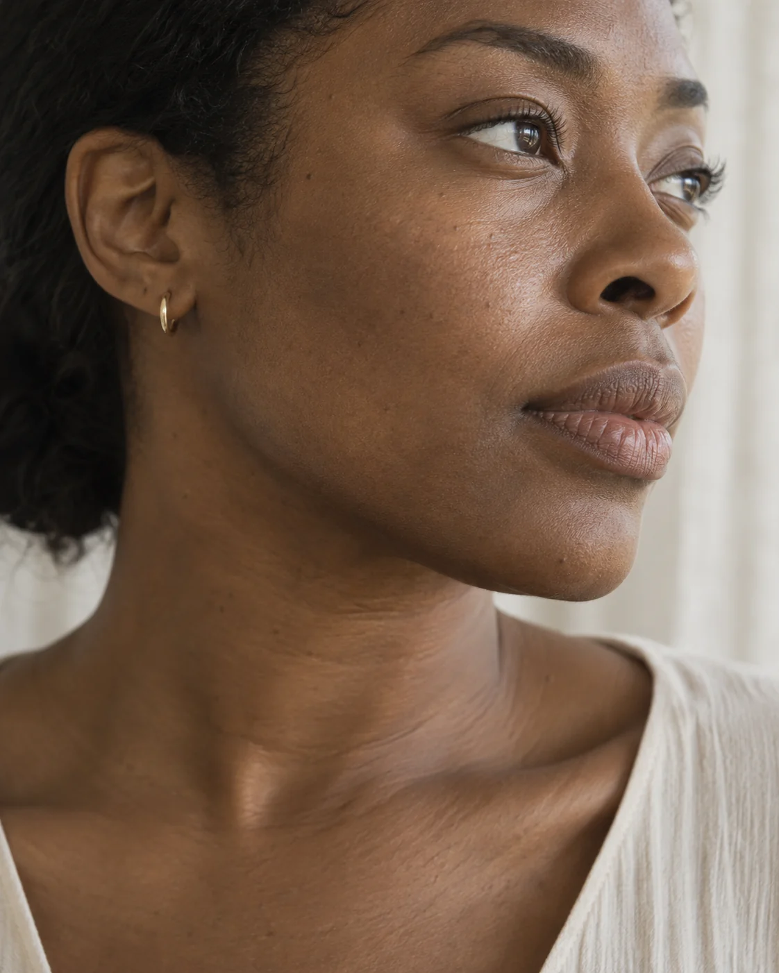 Close-up of a woman's cheek and jawline with natural skin texture in soft daylight